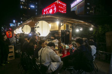 Téléchargez les photos : Fukuoka, Japon ; 1er octobre 2023 : Les gens mangent et boivent dans un Yatai dans la baie d'Hakata. Un Yatai est un petit étal de nourriture mobile au Japon qui vend généralement des ramen ou d'autres aliments.. - en image libre de droit