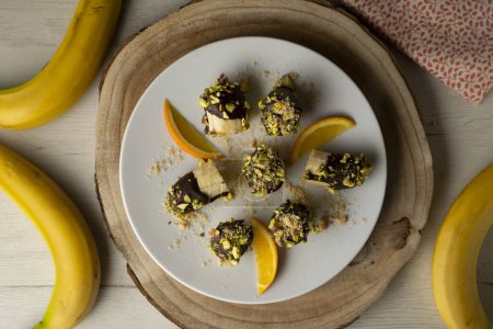 Photo for Banana pieces coated with dark chocolate and pistachios. - Royalty Free Image