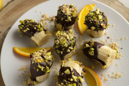 Photo for Banana pieces coated with dark chocolate and pistachios. - Royalty Free Image