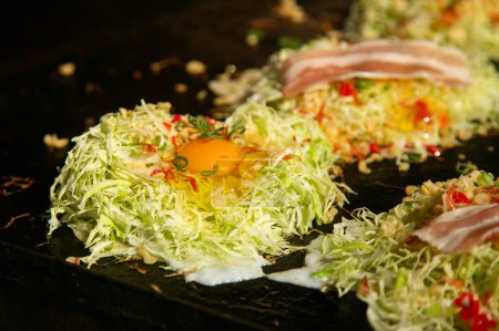 Okonomiyaki es un salado panqueque de col japonesa a la parrilla como te gusta con su elección de proteínas y sabrosos condimentos y coberturas.