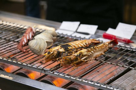 Téléchargez les photos : Coquille de fruits de mer et poisson cuits sur un gril au marché aux poissons d'Osaka au Japon. - en image libre de droit