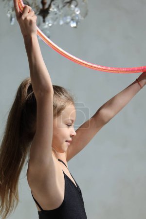 girl gymnast in a black leotard with a with hoop on a grey background. Rhythmic gymnastics concept. High quality photo