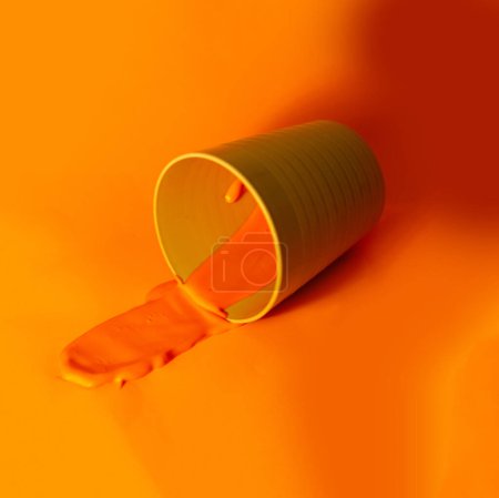 Peinture orange dans une tasse en plastique sur fond orange. Espace de copie.