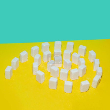 White sugar cubes on a yellow and blue background. Creative concept top view. 