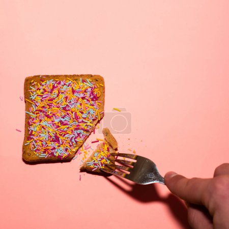 Toast with colorful sprinkles and fork on pink background. Creative food concept. 