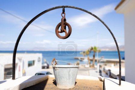 Photo for An old well with a bucket and a blurred sea on the background. - Royalty Free Image