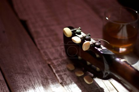 Téléchargez les photos : Tête de caisse d'une guitare acoustique à côté d'un verre de boisson alcoolisée, sur bois blanc vieilli, concept romantique, mélancolique. - en image libre de droit