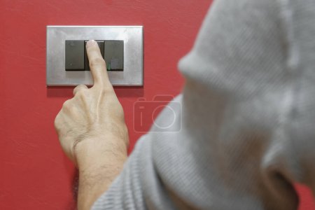 Photo for Close up rear view left hand finger young man turn off grey light switch on leather red wall decoration before going to bed. Eco-friendly at home and electricity bill saving concept. Selective focus. - Royalty Free Image