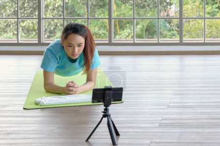Photo for Young asian woman concentrate doing yoga plank pose follow online tutorial from smartphone at home. Young people domestic life concept. Selective focus and copy space. - Royalty Free Image