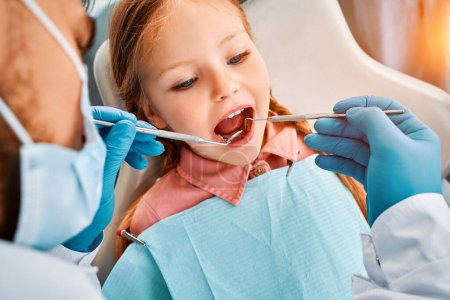 Photo for Close-up portrait of a little girl patient whose teeth are being checked by a dentist. Dental treatment, children's dentistry. - Royalty Free Image