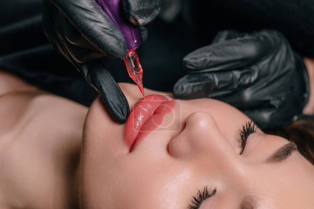 Foto de Permanent lip makeup. The cosmetologist makes the procedure of permanent makeup to the client in the salon. - Imagen libre de derechos