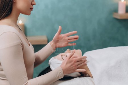 Téléchargez les photos : L'esthéticienne fait un massage facial. La jeune femme s'allonge sur le dos et obtient un lifting dans un salon de spa. Techniques de massage anti-âge. - en image libre de droit