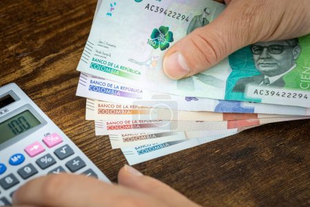 Photo for Man holds Colombian pesos in hand and counts on expenses or earnings calculator, Financial concept, home budget of Colombians - Royalty Free Image
