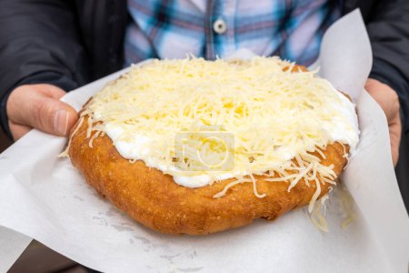 Langos held in hands, Sold in the street, traditional in Eastern Europe, deep-fried dough, Street food served with various toppings, A delicacy known in Hungary, slovakia, czech republic,Romania and Bulgaria