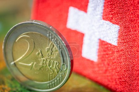 2-Euro-Münze auf dem Hintergrund der Flagge der Schweiz, Konzept, Handelszusammenarbeit, Zwischen dem Euroraum und der Schweiz, Geschäftsbeziehungen des Euro und des Schweizer Franken, Nahaufnahme