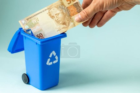 Brazilian money, 50 reais banknote throwing into the trash can, Financial concept, Cashless trend, Gradual withdrawal of cash from the market, Copy space, beautiful blue background