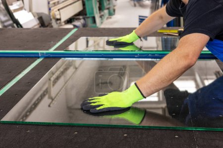 A glazier breaks a panel of glass on a special table in a glass factory