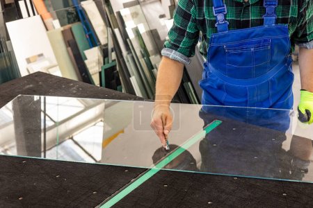 A glazier cuts glass in a glass factory