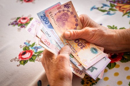 Dinero argentino pesos, una pensionista sostiene varios billetes en su mano, Problemas financieros de personas mayores, inflación y pobreza en Argentin