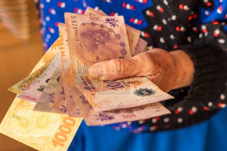 Foto de Dinero argentino, una pensionista tiene varios billetes de pesos en su mano, Problemas financieros de personas mayores, pensiones bajas en Argentina - Imagen libre de derechos