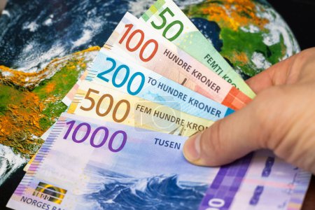 Norwegisches Geld, Wechselkurse, Weltwirtschaft, Finanzunternehmenskonzept, Norwegische Krone in der Hand vor dem Hintergrund der Welt