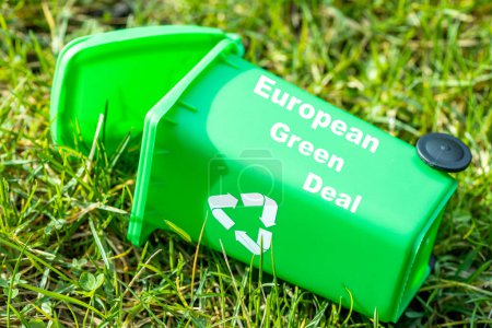 green garbage bin lying in the grass with the text European Green Deal, Environmental concept, Changes in the Green Deal, Farmers' protests, ecological project, close up