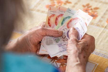 Haushalt älterer Menschen in Singapur. Wirtschaftskonzept, Rentnerin hält mehrere Singapur-Dollar in den Händen, Finanzielle Situation älterer Menschen in Singapur