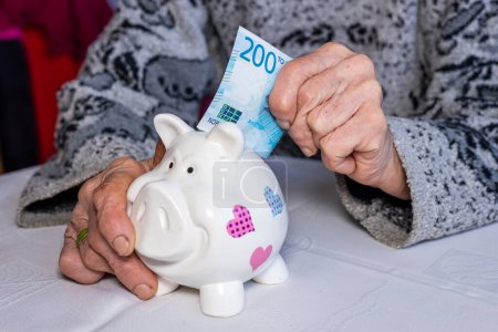 Norwegen Geld, Rentner legt 200 norwegische Kronen in ein Sparschwein, Finanzkonzept, Sparen und finanzielle Sicherheit älterer Menschen