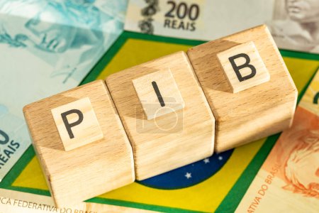 Das Wort PIB (Bruttoinlandsprodukt) steht auf Holzwürfeln mit einigen brasilianischen Real-Banknoten auf gelben, grünen und blauen Nationalsymbolen Brasiliens. Brasilianisches Portugiesisch