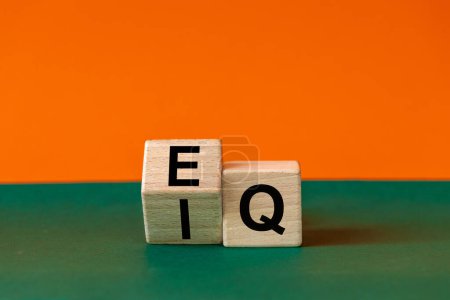 Icono EI o EQ. Un bloque de madera con una palabra que muestra tanto el símbolo de la inteligencia emocional como el cociente emocional. Hermoso fondo verde y naranja, espacio para copiar. Psicológico e IE o EQ