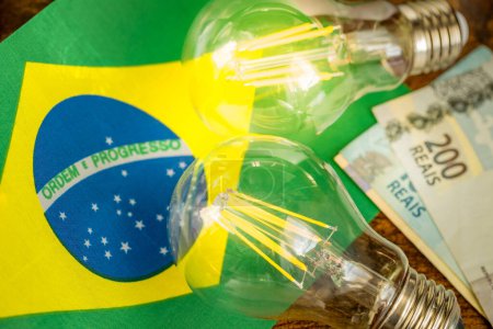 Stromkosten in Brasilien, wirtschaftliches und finanzielles Konzept. Brasilianische Flagge, zwei brennende Glühbirnen und Geld