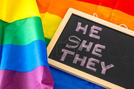 HE SHE THEM Handwritten in chalk on a school blackboard, concept on the background of a rainbow flag gender Rights of non-binary transgender people. Support for the LGBTQ community, gender tolerance and equal rights