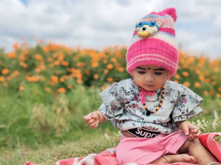 Téléchargez les photos : Mignon bébé fille Gros plan portrait portant chapeau rose et robe verte dans les terres agricoles de fleur de souci - en image libre de droit