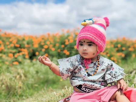 Téléchargez les photos : Mignon bébé fille Gros plan portrait portant chapeau rose et robe verte dans les terres agricoles de fleur de souci - en image libre de droit