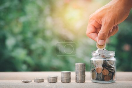 Man's hand putting coins in a glass jar, stacks of coins representing growth, future savings growth concept, financial and banking.