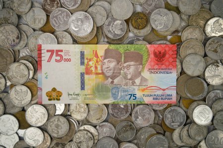 Foto de Yogyakarta, Indonesia - January 06, 2023: Special edition paper money for 75 years of Indonesian independence (rupiah) on a pile of coins of various shapes, year of manufacture and value. - Imagen libre de derechos