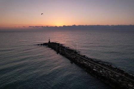 Téléchargez les photos : Colorful drone image of the sun rising over the horizon with a small lighthouse silhouette on a breakwater - en image libre de droit