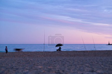 Téléchargez les photos : Horizontal tranquil scene at the beach during a blue Fall sunset with fishermens silhouette. High-quality photo - en image libre de droit