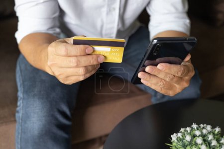 Photo for Man holding credit card and using smartphone at home, businessman shopping online, e-commerce, internet banking, spending money, working from home concept, Sit on the sofa in the living room at home. - Royalty Free Image