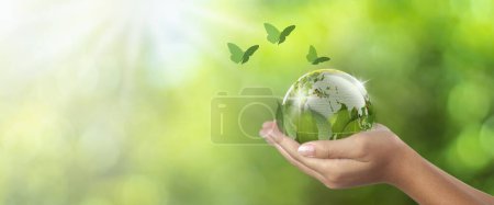 Environmental conservation earth concept, woman holding globe under leaf and butterfly flying nearby, earth in woman's hand green bokeh background and white light