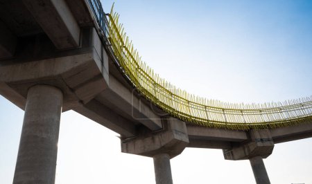 Foto de Una fotografía de ángulo bajo de una pasarela peatonal de hormigón con rieles metálicos amarillos, que muestra elementos de ingeniería de hormigón robustos - Imagen libre de derechos