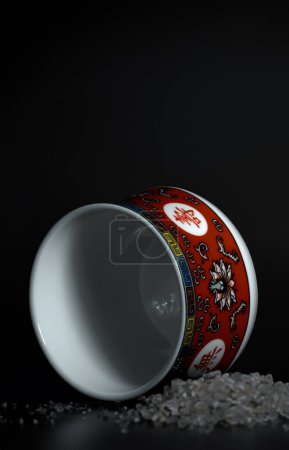 Photo for A red oriental teacup placed next to sugar crystals on a black background. - Royalty Free Image