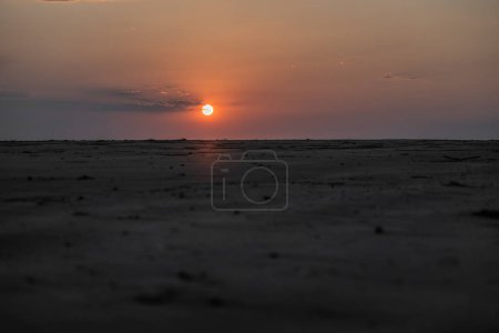 Téléchargez les photos : Le soleil se couche à l'horizon derrière une colline de plage de sable fin en Australie, créant une atmosphère de l'autre monde. - en image libre de droit