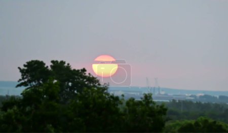 Téléchargez les photos : Le soleil couchant est divisé en deux en passant des nuages pendant qu'il descend sur le port. - en image libre de droit