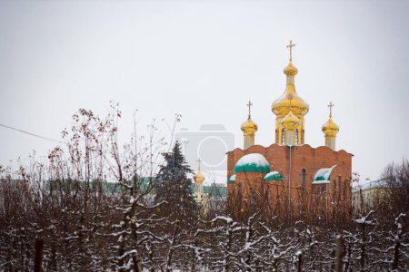 Foto de Una gran iglesia ortodoxa en invierno sobre el fondo de un bosque de invierno. Cúpulas doradas bajo el cielo. Ambiente de iglesia - Imagen libre de derechos