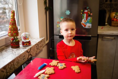 Foto de Bright homemade Christmas cookies in the children's hands of a 4-year-old boy. Santa is waiting at home - Imagen libre de derechos