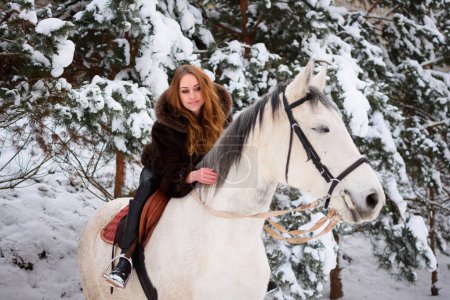 Foto de A 25-year-old Ukrainian girl riding a white horse. Christmas vacation and travel. Active recreation in the forest - Imagen libre de derechos