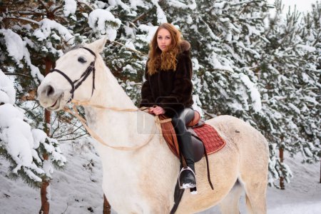 Téléchargez les photos : Winter coniferous forest with snow. A young girl with long hair in a fur coat riding a horse. Christmas atmosphere and holidays - en image libre de droit