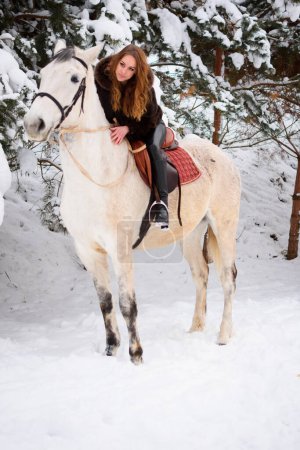 Téléchargez les photos : A 25-year-old Ukrainian girl riding a white horse. Christmas vacation and travel. Active recreation in the forest - en image libre de droit