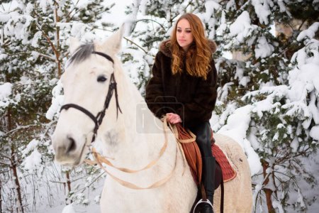 Foto de Winter coniferous forest with snow. A young girl with long hair in a fur coat riding a horse. Christmas atmosphere and holidays - Imagen libre de derechos